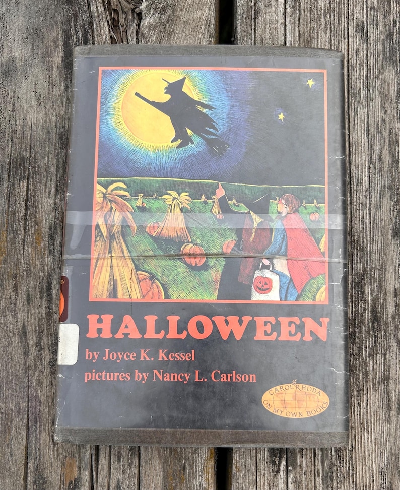 Może przedstawiać: Książka w twardej oprawie zatytułowana Halloween autorstwa Joyce K. Kessel z ilustracjami Nancy L. Carlson. Okładka przedstawia czarną sylwetkę czarownicy lecącej na miotle na tle dużego ż&oacute;łtego księżyca, nad polem z dyniami i dwiema postaciami.