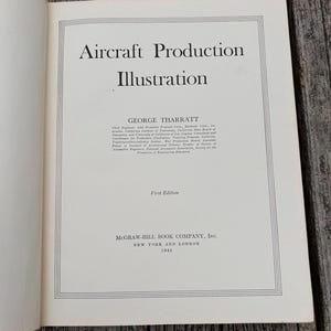 Pu&ograve; includere: La pagina del titolo del libro del 1944 Aircraft Production Illustration di George Tharratt, pubblicato da McGraw-Hill Book Company, Inc. a New York e Londra. Il testo &egrave; stampato in inchiostro nero su una pagina bianca con un bordo a doppia linea.