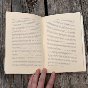 Puede incluir: Un libro de tapa dura abierto con p&aacute;ginas de color crema y texto impreso en negro. La p&aacute;gina izquierda se titula Famous American Indians y la derecha Crazy Horse, con los n&uacute;meros de p&aacute;gina 58 y 59 visibles en la parte inferior.