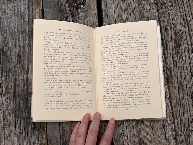 Puede incluir: Un libro de tapa dura abierto con p&aacute;ginas de color crema y texto impreso en negro. La p&aacute;gina izquierda se titula Famous American Indians y la derecha Crazy Horse, con los n&uacute;meros de p&aacute;gina 58 y 59 visibles en la parte inferior.