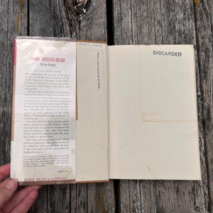 Puede incluir: Un libro de tapa dura titulado Famous American Indians de William Heuman con una sobrecubierta que presenta texto hist&oacute;rico. La p&aacute;gina interior tiene la palabra DISCARDED impresa en tinta negra. El libro est&aacute; abierto, mostrando la solapa.