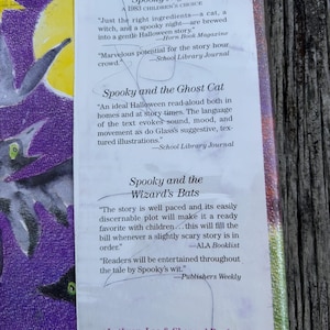 K&ouml;nnte beinhalten: Ein Buchcover mit violettem Hintergrund, einem gelben Mond und schwarzen Fledermausillustrationen. Der Text enth&auml;lt die Titel Spooky Night, Spooky and the Ghost Cat und Spooky and the Wizard's Bats sowie Rezensionen und den Verlagsnamen.