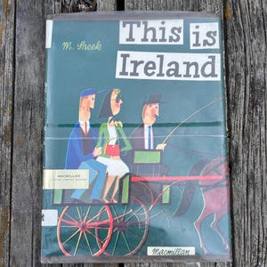 Peut inclure: Un livre reli&eacute; intitul&eacute; This is Ireland par M. Sasek, pr&eacute;sentant une couverture verte avec une illustration stylis&eacute;e de trois personnes dans une cal&egrave;che tir&eacute;e par un cheval. Le logo Macmillan Master Library Edition est visible.