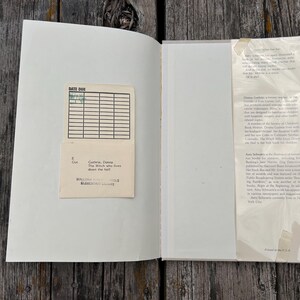 Puede incluir: Un libro de tapa dura abierto con una tarjeta de biblioteca de color crema pegada en la cubierta interior izquierda. La tarjeta presenta una cuadr&iacute;cula para fechas y el texto Guthrie, Donna, The Witch who lives down the hall. A la derecha, una solapa.