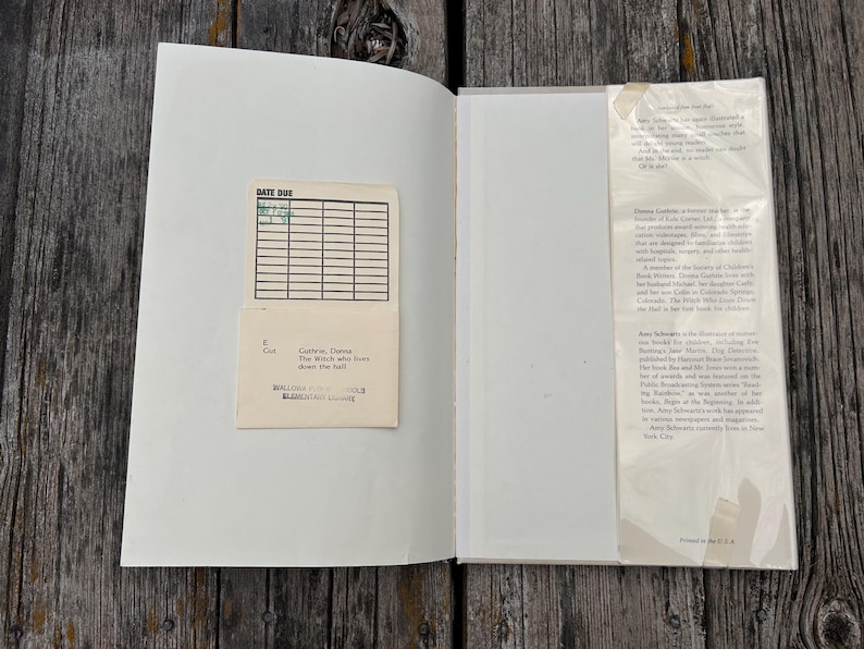 Puede incluir: Un libro de tapa dura abierto con una tarjeta de biblioteca de color crema pegada en la cubierta interior izquierda. La tarjeta presenta una cuadr&iacute;cula para fechas y el texto Guthrie, Donna, The Witch who lives down the hall. A la derecha, una solapa.