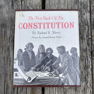 Puede incluir: Un libro de tapa dura titulado The First Book Of The Constitution de Richard B. Morris con ilustraciones de Leonard Everett Fisher. La cubierta blanca presenta una ilustraci&oacute;n en blanco y negro de figuras hist&oacute;ricas firmando.