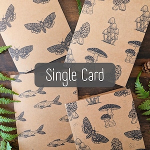 May include: Greeting cards with various black illustrations on a brown background. Designs include moths, mushrooms, and fish. The text "Single Card" is displayed on a black rectangle.