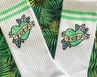 May include: White socks with green stripes and a green heart with the word "TOFU" in a tattoo style design. The socks also have a green lightning bolt with the words "TOFU" and "VEGAN" on the bottom.
