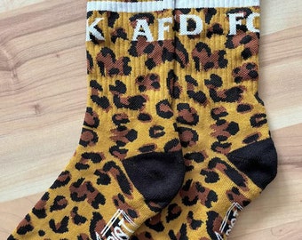 May include: A pair of black and yellow socks with a leopard print design. The socks have a white stripe and the text "KAFD FC" on the top. The bottom of the socks have the text "GREEN LIGHT" in white.