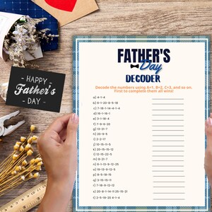 May include: A Father's Day decoder activity sheet with a blue plaid border, featuring the text FATHER'S DAY DECODER and a list of numbered clues to solve using a simple A=1, B=2, C=3 cipher. The sheet is held against a wooden background.