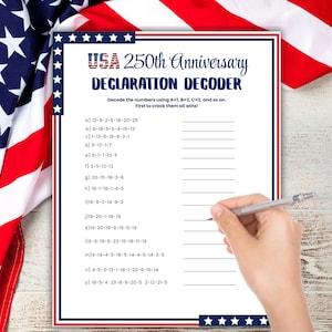 May include: A white sheet with the text "USA 250th Anniversary DECLARATION DECODER" and a list of numbered letter codes. A hand holds a silver pen, ready to solve the puzzle. The American flag is in the background.