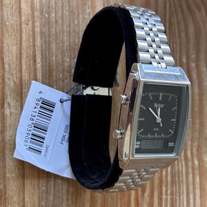 May include: A silver Pulsar watch with a rectangular black face, showing both analogue and digital time. The watch has a metal strap and is displayed on a black stand. A price tag is attached.
