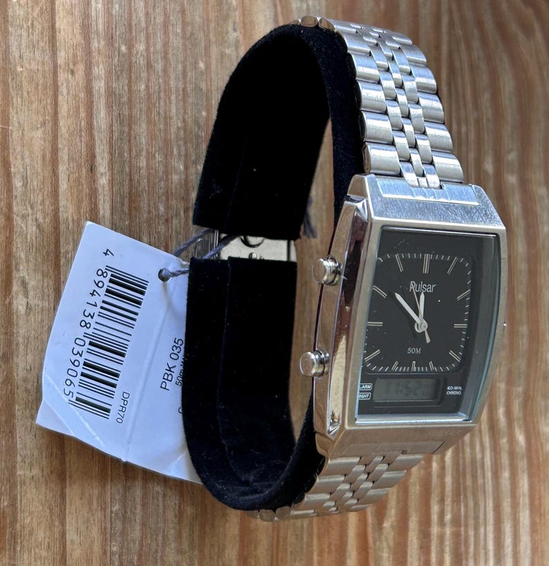 May include: A silver Pulsar watch with a rectangular black face, showing both analogue and digital time. The watch has a metal strap and is displayed on a black stand. A price tag is attached.