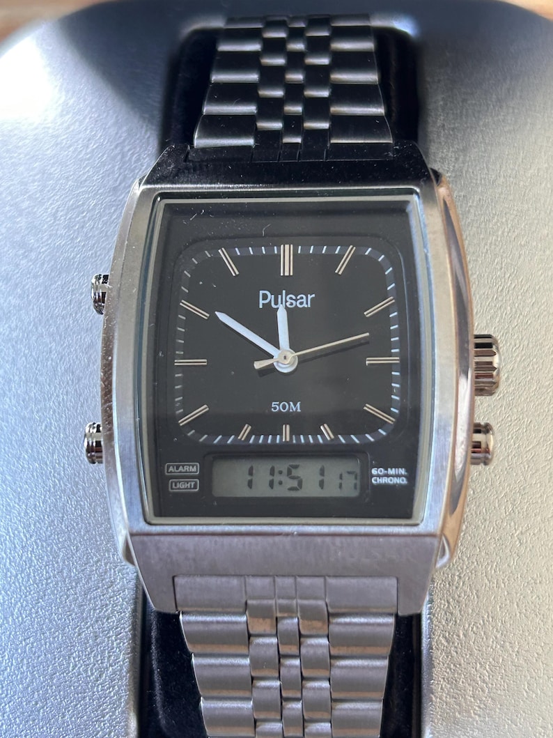 May include: Silver Pulsar watch with a black face and a rectangular design. The watch features a digital display showing "11:51 17" and analog hands. The watchband is made of linked metal. The watch has two side buttons.