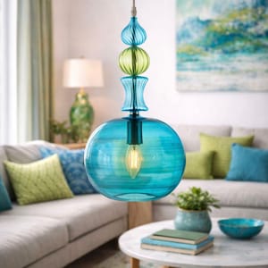 Puede incluir: Lámpara colgante de cristal turquesa con elementos decorativos azules y verdes. La lámpara está suspendida de un soporte de techo plateado. La luz está encendida, iluminando un salón. El globo tiene unos 30 cm de diámetro.