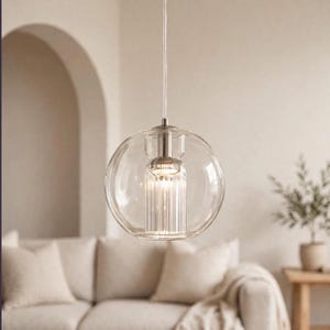 May include: A spherical pendant light fixture featuring a clear glass outer globe and a central cylindrical fluted glass insert. The light is suspended by a thin white cord and includes a metallic silver-toned hardware cap at the top.