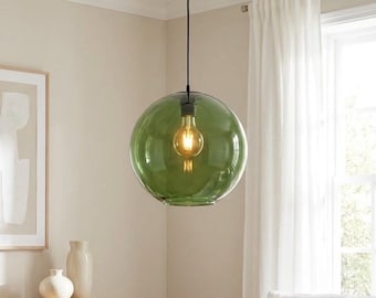 May include: A spherical pendant light fitting featuring a translucent olive green glass shade suspended by a thin black cord. The lamp contains a single glowing Edison-style light bulb visible through the clear, rounded glass globe.
