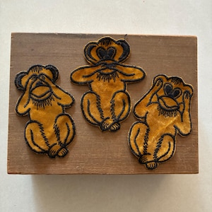 May include: Three embroidered patches featuring monkeys in the see-no-evil, hear-no-evil, and speak-no-evil poses. Each patch is crafted from a mustard yellow fabric with detailed black thread embroidery outlining the monkey figures.