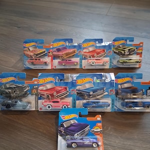May include: A collection of Hot Wheels die-cast model cars in their original packaging. The cars are various colors, including red, pink, blue, and purple. The packaging features the Hot Wheels logo and car model names.