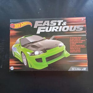 May include: A Hot Wheels die-cast car set featuring the Fast & Furious franchise. The box displays a green Mitsubishi Eclipse model car with black accents. The packaging includes a list of other car models.