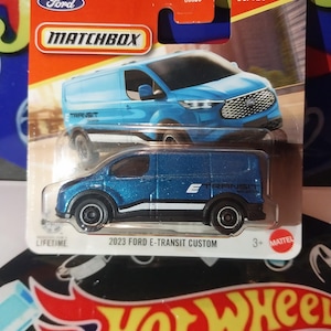 May include: A Matchbox die-cast model of a 2023 Ford E-Transit Custom van. The van is blue with black and white accents, and the packaging includes the Ford and Matchbox logos. The model is part of the 36/125 series.