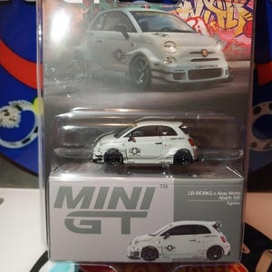 May include: A white Mini GT model car of a Fiat 500 Abarth 595, with black wheels and Liberty Walk branding. The packaging includes the Mini GT logo and the text "LB-WORKS x Abas Works Abarth 595 Fighters".