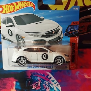 May include: A white 2018 Honda Civic Type R die-cast model car on a blue and orange Hot Wheels card. The car has black wheels and a black graphic on the side. The card features the Hot Wheels logo and Night Speed branding.