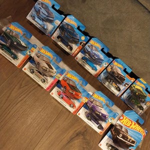 May include: A collection of Hot Wheels toy cars in their original packaging. The cars are various colors, including blue, green, orange, and black. The packaging is blue and features the Hot Wheels logo.