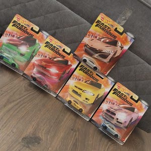 Puede incluir: Una colección de seis coches de juguete Hot Wheels Fast & Furious en su embalaje original. Los coches son de varios colores, incluyendo verde, rojo, amarillo y rosa. Cada paquete presenta el logotipo de Fast & Furious.