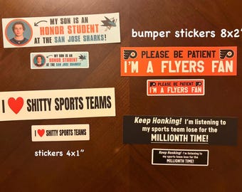Puede incluir: Una colección de pegatinas rectangulares con textos sobre deportes. Los diseños incluyen My Son Is An Honor Student At The San Jose Sharks, Please Be Patient I'm A Flyers Fan, I Heart Shitty Sports Teams y Keep Honking! I'm listening to my sports team lose for the millionth time. Las dimensiones 20,32x5,08 cm y 10,16x2,54 cm están impresas en la imagen.
