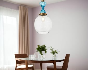 May include: A clear glass pendant light with a patterned globe shade and a turquoise blue decorative top. The light fixture hangs above a round wooden table with chairs. The room has a neutral color palette.