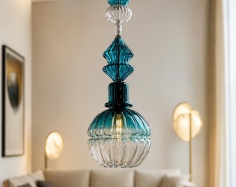 May include: A pendant light fixture featuring a series of stacked, ribbed glass elements in shades of teal and clear glass. The design includes a large, rounded, fluted glass shade at the bottom, topped with a diamond-shaped piece and two spheres.