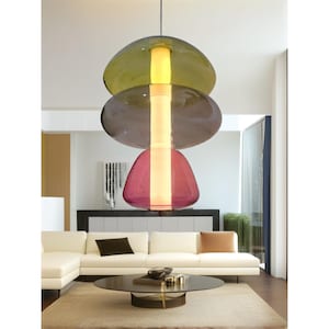 Könnte beinhalten: Eine moderne, mehrschichtige Pendelleuchte mit drei Glasschirmen in den Farben Lila, Grau und Gelb. Die Leuchte hängt von der Decke in einem Wohnzimmer.
