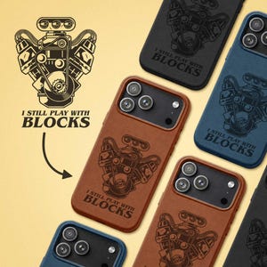 May include: A collection of smartphone cases in black, blue, and brown, each featuring a detailed black line art illustration of a V8 engine and the text "I STILL PLAY WITH BLOCKS" printed on the back surface near the camera module.