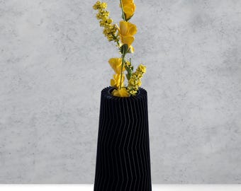 May include: A black, geometric vase with a wavy, textured design holds a bouquet of yellow flowers.