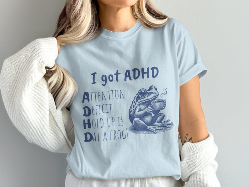 Pode incluir: Camiseta azul claro com um gr&aacute;fico de sapo azul e o texto "Eu tenho TDAH. D&eacute;ficit de aten&ccedil;&atilde;o Hold Up Is Dat A Frog?"