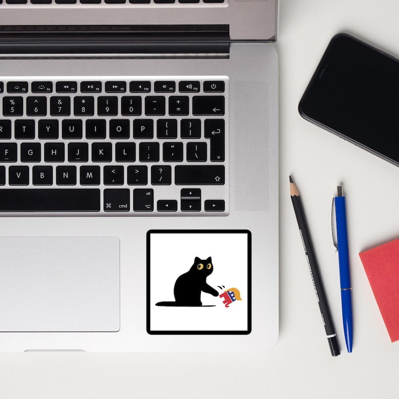Puede incluir: Una pegatina de gato negro con ojos amarillos y un gr&aacute;fico rojo, blanco y azul. El gato est&aacute; alcanzando el gr&aacute;fico. La pegatina es cuadrada y tiene un fondo blanco. La pegatina est&aacute; sobre una superficie blanca.
