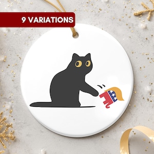 Può includere: Ornamento natalizio rotondo in ceramica bianca con un gatto nero che colpisce un elefante rosso, bianco e blu con un parrucchino biondo. Il ciondolo ha un cordino dorato per appenderlo e uno striscione rosso con testo.