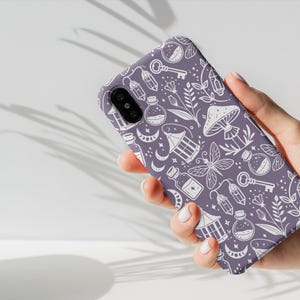 K&ouml;nnte beinhalten: Lilafarbener Handy-Case mit einem wei&szlig;en Design aus verschiedenen magischen Gegenst&auml;nden, darunter Schl&uuml;ssel, Flaschen, Pilze und Laternen.