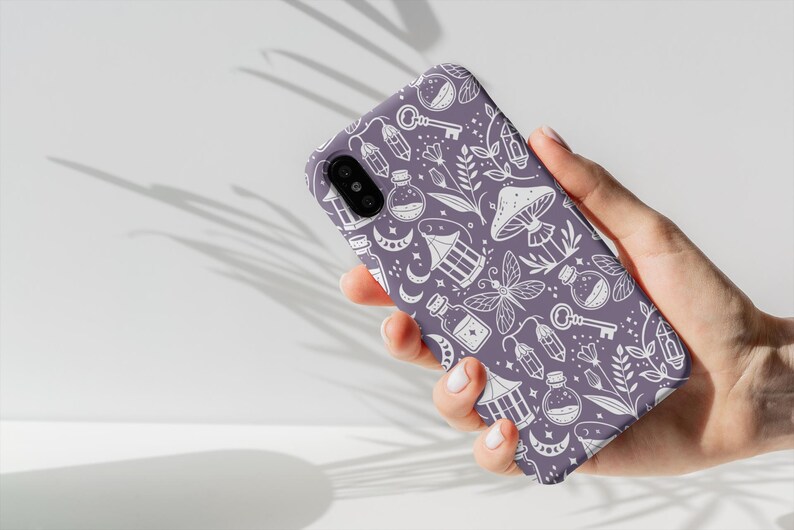 K&ouml;nnte beinhalten: Lilafarbener Handy-Case mit einem wei&szlig;en Design aus verschiedenen magischen Gegenst&auml;nden, darunter Schl&uuml;ssel, Flaschen, Pilze und Laternen.
