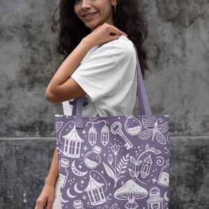 K&ouml;nnte beinhalten: Eine lilafarbene Einkaufstasche mit einem wei&szlig;en Design aus verschiedenen magischen Gegenst&auml;nden, darunter Flaschen, Laternen, Pilze und ein Schl&uuml;ssel. Das Design wiederholt sich auf der gesamten Tasche.