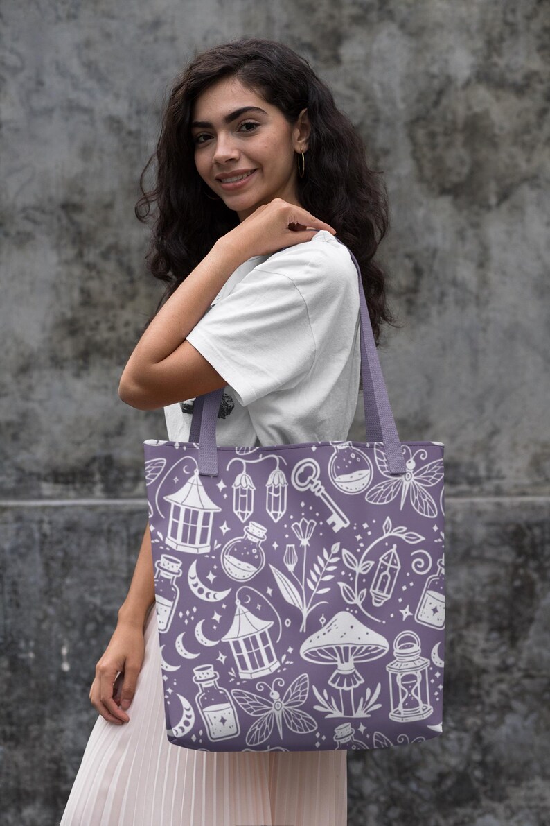 K&ouml;nnte beinhalten: Eine lilafarbene Einkaufstasche mit einem wei&szlig;en Design aus verschiedenen magischen Gegenst&auml;nden, darunter Flaschen, Laternen, Pilze und ein Schl&uuml;ssel. Das Design wiederholt sich auf der gesamten Tasche.