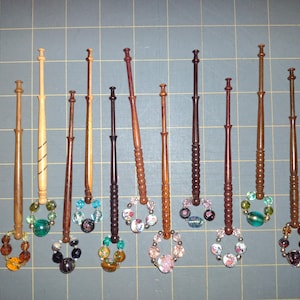 Puede incluir: Una colección de 12 agujas de tejer de madera con adornos de cuentas de colores. Las agujas son de diferentes longitudes y tienen cuentas de diferentes colores.