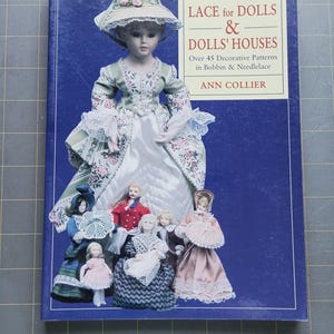 Peut inclure: Un livre intitulé "Lace for Dolls & Dolls' Houses" avec une couverture bleue. La couverture présente une poupée dans une robe verte et blanche et une collection de poupées miniatures. Le titre du livre et l'auteur, Ann Collier, sont également visibles.