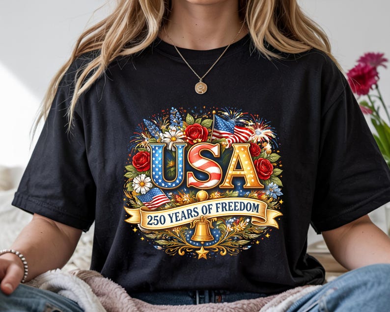 May include: Black t-shirt featuring a patriotic design with the word "USA" in red, white, and blue, surrounded by flowers, flags, and fireworks. The text "250 YEARS OF FREEDOM" is displayed on a banner below.