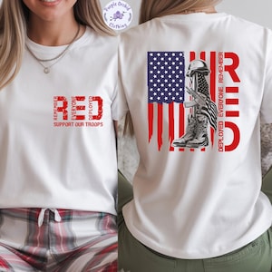 May include: White t-shirt with a red graphic on the front that says "RED" and "SUPPORT OUR TROOPS". The back of the shirt features an American flag design with a helmet, rifle, and boots. The text "RED" and "REMEMBER EVERYONE DEPLOYED" is also on the back.
