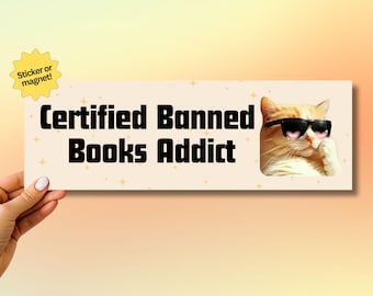 May include: A sticker or magnet with a cat wearing sunglasses and the text "Certified Banned Books Addict" on a peach background with gold glitter.