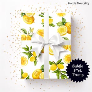 May include: A wrapped gift with a white bow, featuring a lemon pattern with the text "F*ck Trump". The lemons are yellow with green leaves on a white background. The gift is decorated with gold confetti and a black starburst with the text "Subtle F*ck Trump".