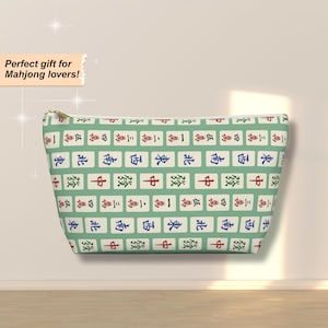 May include: A rectangular cosmetic bag with a repeating pattern of Mahjong tiles in red, blue, and green on a light green background. The bag has a gold zipper and is designed for Mahjong lovers.