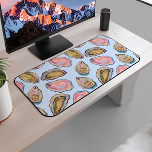 May include: A rectangular mouse pad with a light blue background and a pattern of watercolor oyster illustrations in shades of pink, gold, and brown. The mouse pad is on a light-colored desk, near a computer monitor.